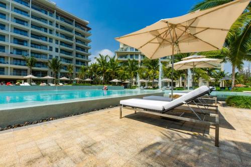 a pool with a beach chair and an umbrella at Sunshine Apartment in 5* resort in Da Nang