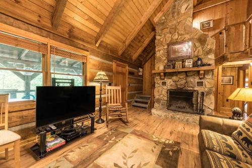 a living room with a large television and a stone fireplace at Authentic log home with hot tub, fireplace, fire pit and billiards ! in Gatlinburg
