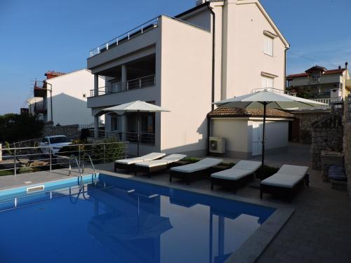 einem Pool mit Bänken und einem Sonnenschirm neben einem Gebäude in der Unterkunft Apartments Villa Residenca in Novi Vinodolski