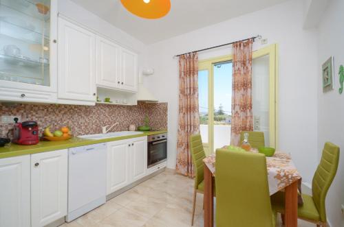a kitchen with white cabinets and a table with green chairs at Kapris House in Agios Prokopios