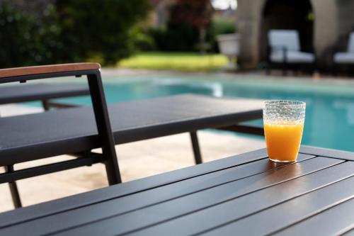 un verre de jus d'orange assis sur une table à côté d'une piscine dans l'établissement L'Hote Antique - MAISON D'HOTE- 4 Suites avec cuisine, à Pichanges