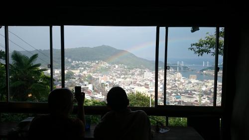 two people taking a picture of a city with a rainbow at Onomichi Guest House Miharashi-tei in Onomichi