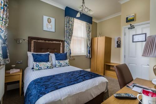 a bedroom with a bed with blue sheets and a desk at The Golden Lion Hotel, St Ives, Cambridgeshire - The Coaching Inn Group in St Ives