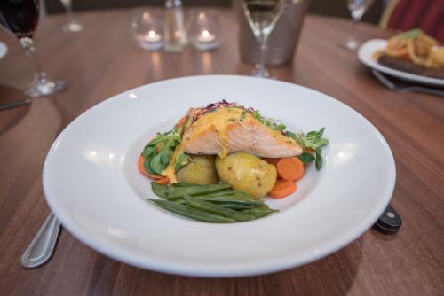 a white plate with a fish and vegetables on a table at Alexandra Hotel in Fort William