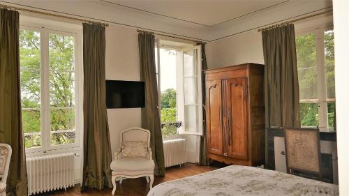 a bedroom with a bed and a chair and windows at B&B Château de Preuil in Vallenay
