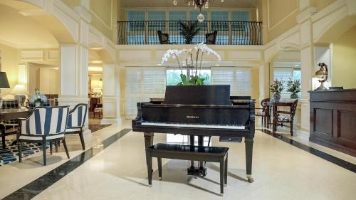 a piano in a living room with chairs and a table at Inn at Pelican Bay in Naples
