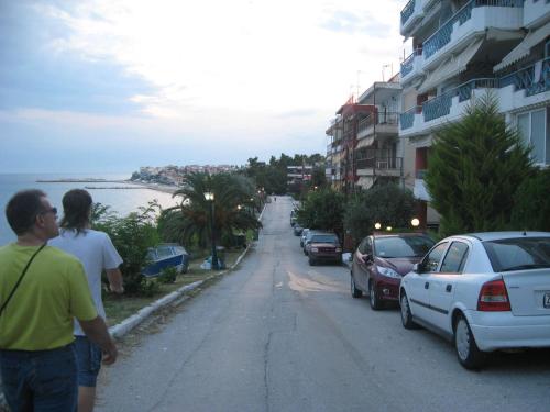 two people walking down a street with cars parked at Hotel Paraktio in Nea Kalikratia