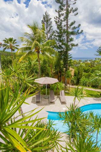 a pool with an umbrella and chairs and trees at Carre Royal in Deshaies