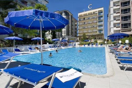 una gran piscina con sillas y sombrillas azules en Hotel Caravelle, en Cattolica