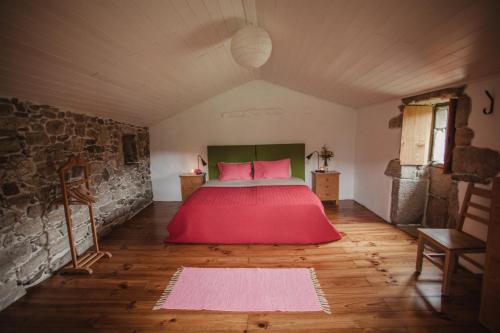 1 dormitorio con cama roja y pared de piedra en O Curralino, en Vilacoba