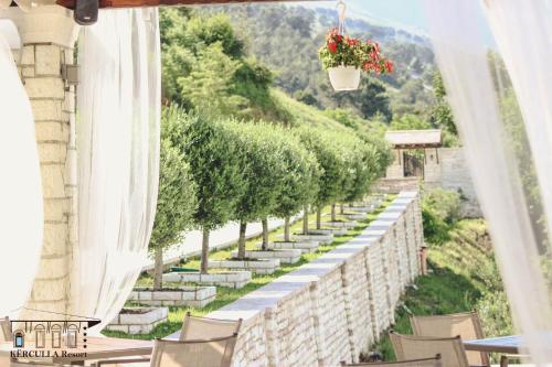 a row of tables and chairs on a wall with trees at KERCULLA Resort in Gjirokastër