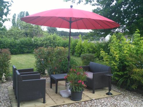 a patio with a red umbrella and chairs and a table at La cité des abeilles in Villemandeur