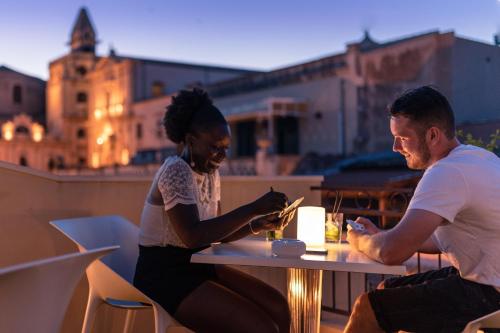 a man and a woman sitting at a table on their cell phones at Hotel Porta Reale in Noto