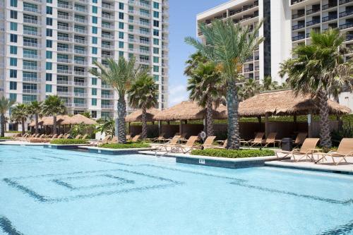 a swimming pool with chairs and palm trees and buildings at Sapphire in South Padre Island