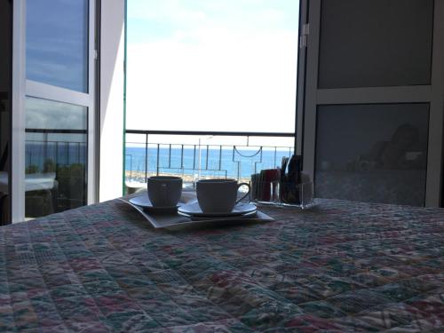 two coffee cups sitting on a bed with a view of the ocean at Baia dei Gabbiani in San Lorenzo al Mare