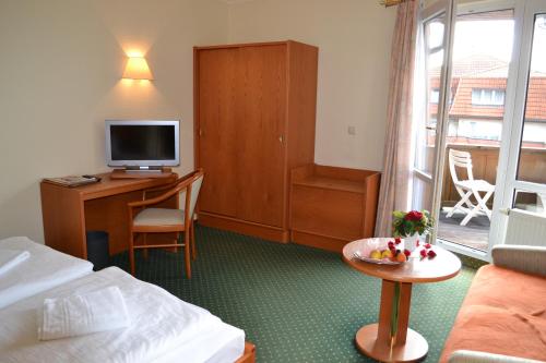 Habitación de hotel con cama y escritorio con TV. en Hotel Garni Seeschlösschen en Kolpinsee