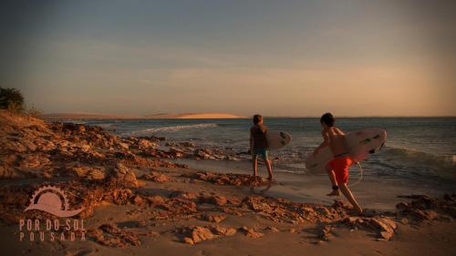 two people walking on the beach with their surfboards at Pousada Por do Sol in Jericoacoara