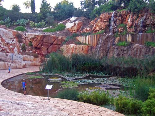 a person standing next to a pond with a waterfall at Zimmer In The Garden in Karmiel