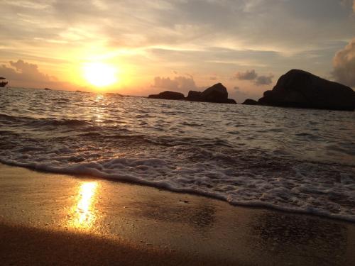 un coucher de soleil sur la plage avec des rochers dans l'eau dans l'établissement Poseidon Resort, à Koh Tao