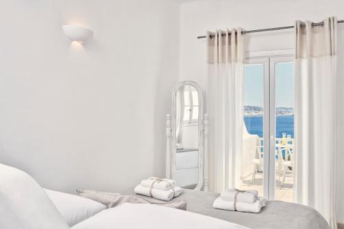 a white room with a bed and a view of the ocean at Mykonos Princess Hotel in Agios Stefanos