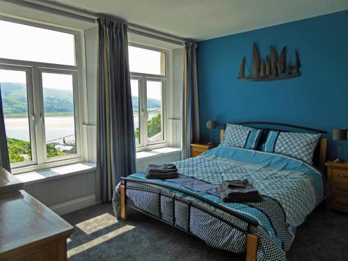 a bedroom with a bed with blue walls and windows at Bryn Melyn Apartments in Barmouth