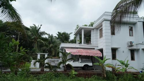 a white house with a red and white awning at Kannur Beachway Homestay in Pāppinisseri