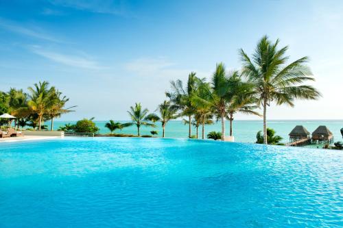 een zwembad met palmbomen en de oceaan bij Melia Zanzibar in Kiwengwa