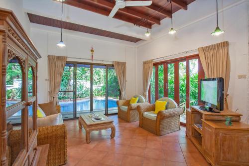 a living room with a tv and a couch and chairs at Traditional Thai Villa Nikkie in Tropical Nature, 4BR & Pool, near Rawai Beach in Nai Harn Beach