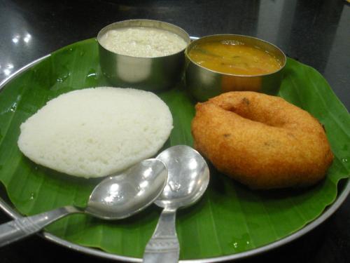 a plate of food with rice and a doughnut on a banana leaf at Wind chimes in Auroville