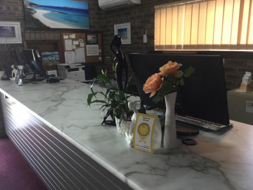 um balcão de escritório com um computador e flores nele em Bayview Motel em Esperance