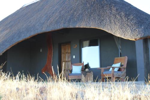 a thatch roofed house with two chairs and a table at Ai Aiba - The Rock Painting Lodge in Omaruru