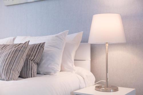 a bed with white pillows and a table with a lamp at Peebles House - Coorie Doon Apartments in Ayr