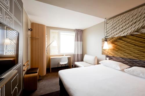 a hotel room with a white bed and a tv at ibis Lyon Carre De Soie in Vaulx-en-Velin