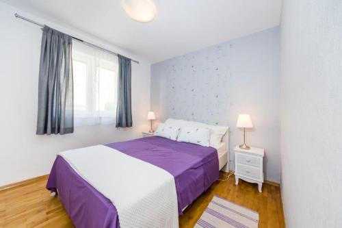 a bedroom with a purple and white bed and a window at Apartmani Paradise in Petrcane