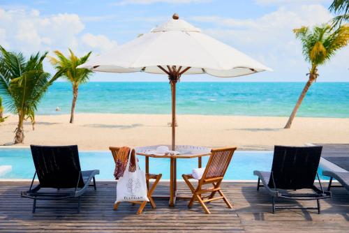 a table with chairs and an umbrella on the beach at The Ellysian Boutique Hotel in Placencia Village