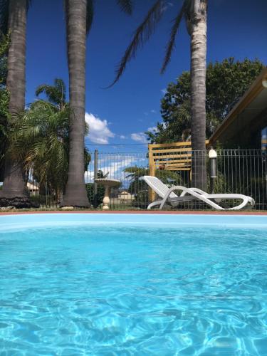 a swimming pool with a chair and palm trees at Lazy Acre Log Cabins in Lakes Entrance