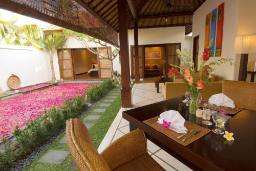 a dining room with a table and a garden with pink flowers at Ellora Villa in Sanur