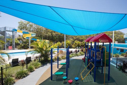 a playground under a blue umbrella next to a pool at Nobby Beach Holiday Village in Gold Coast