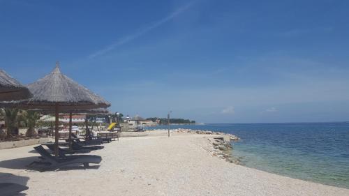a beach with chairs and umbrellas and the ocean at Apartments Elena in Ugljan