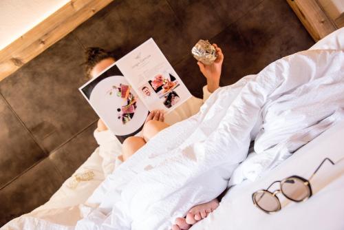 a woman laying in bed reading a magazine at Gourmet AlpinHotel Sonnleiten in Cadipietra