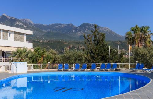a swimming pool with chairs and mountains in the background at Kardamili Beach Hotel in Kardamyli