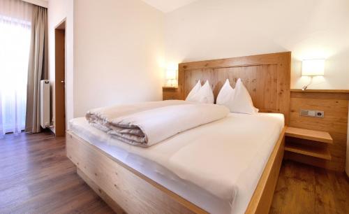 a bedroom with a large white bed with a wooden headboard at Aparthotel Garni Monte in Kartitsch