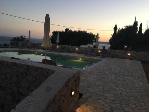 a swimming pool with an umbrella and a stone wall at Anna Studios in Lourdhata