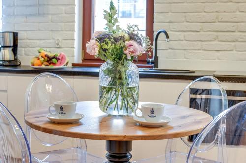 a vase of flowers sitting on a table with two cups at GRANO APARTMENTS Gdańsk Motława SPA & Wellness in Gdańsk