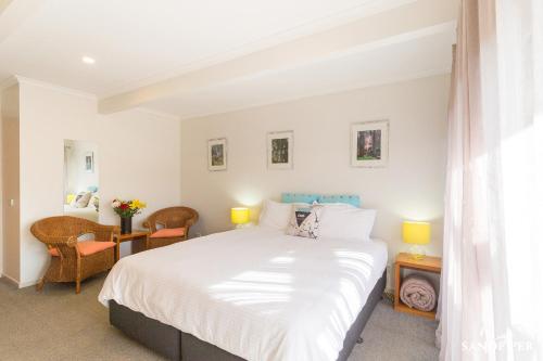 Sandpiper Motel Apollo Bay في خليج أبولو: غرفة نوم مع سرير أبيض كبير وكراسي