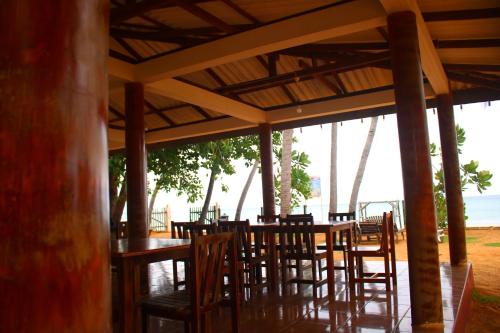 Under Water Safaris and Resort في ترينكومالي: مطعم به طاولات وكراسي خشبية والمحيط