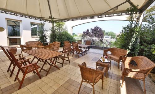 eine Terrasse mit Holztischen, Stühlen und einem Sonnenschirm in der Unterkunft Best Western Classic Hotel in Reggio nell'Emilia