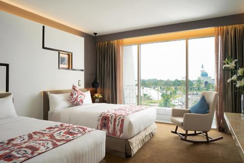 セパンにあるモーベンピック ホテル＆コンベンションセンター KLIAのベッド2台、椅子、窓が備わるホテルルームです。