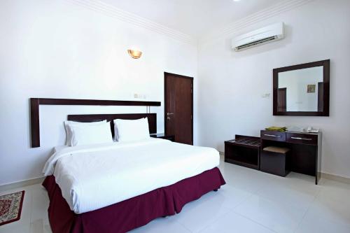 a white bedroom with a large bed and a mirror at Star Emirates Furnished Apartments 2 in Salalah