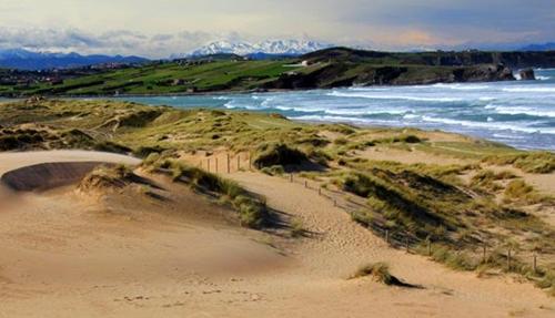 a sandy beach with the ocean and mountains in the background at Casa Boo de Piélagos - Playa de Liencres in Boó de Piélagos